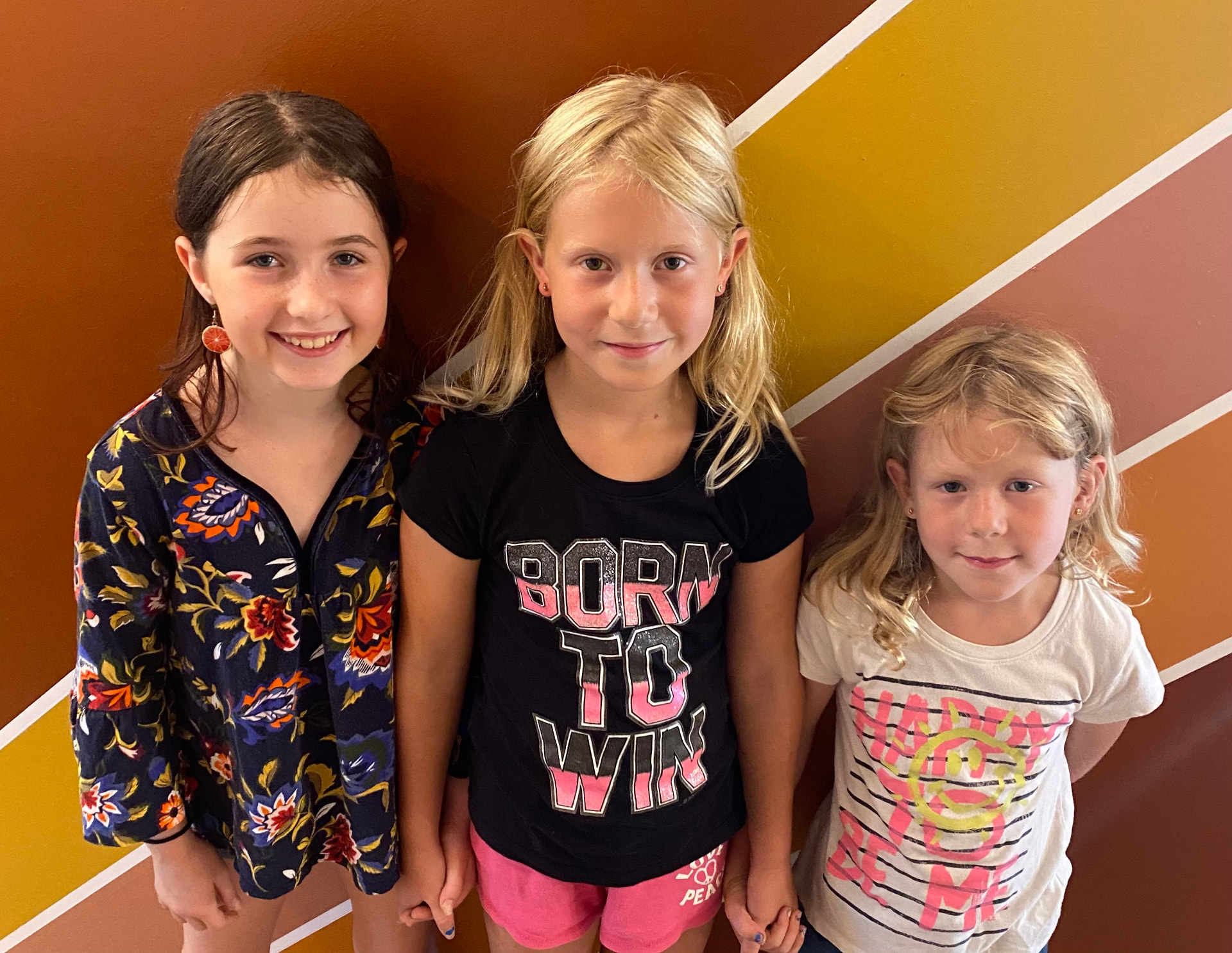 Three happy friends showing off their new piercings by the sunburst mural