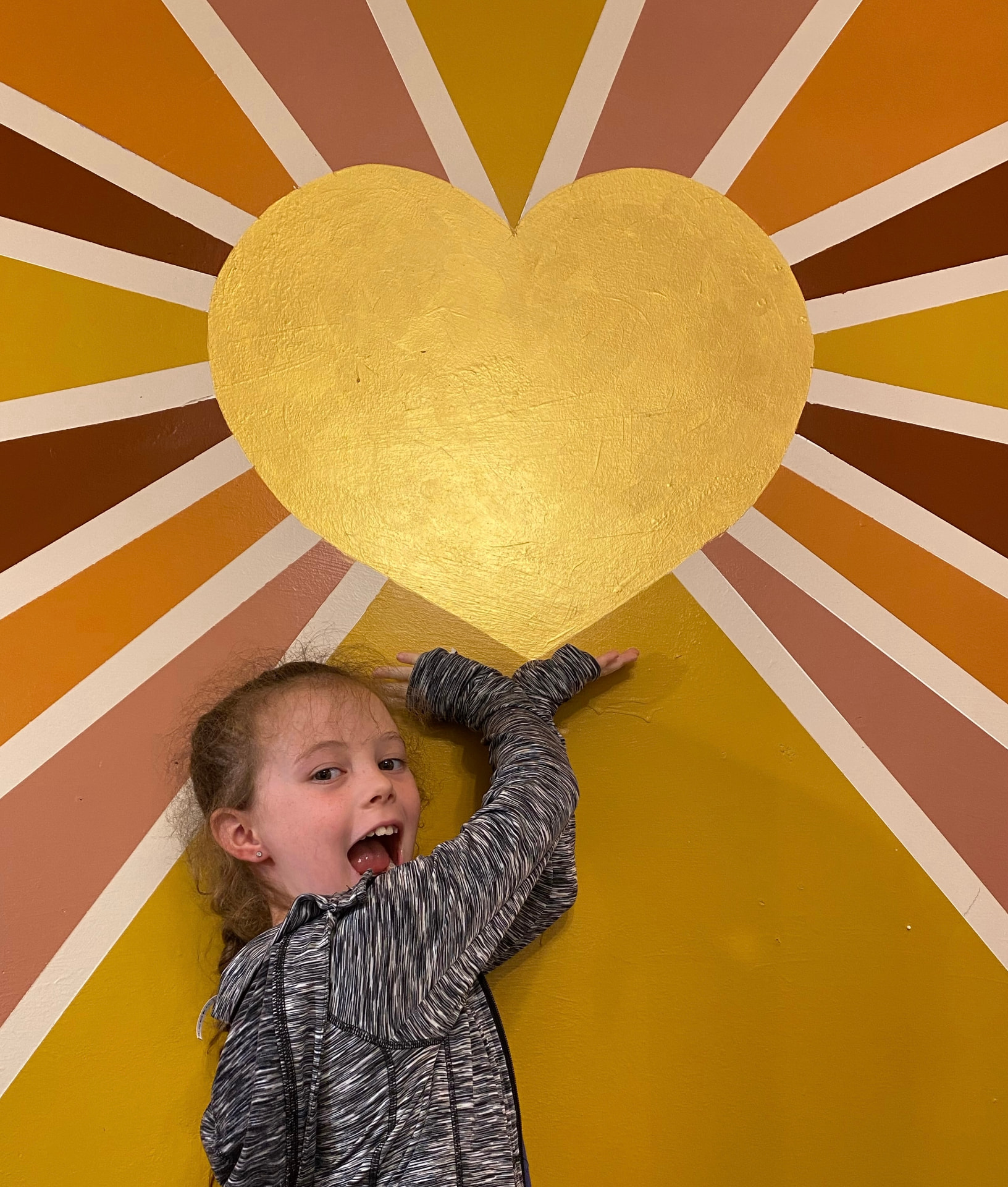 Happy child reaching up toward the gold heart on the sunburst mural